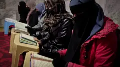 A row of seated women with their faces covered study the holy scriptures.