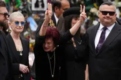 Sharon Osbourne con los dedos de las manos en símbolo de paz hacia los fanáticos presentes en el funeral