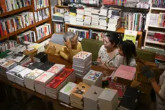 A editora independente Leslie Ng falando com jornalistas na Livraria Hunter, cercada por pilhas de livros e prateleiras repletas.