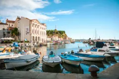 Piran, na Eslovênia. Porto com barcos, em meio à cidade histórica com seus edifícios tradicionais, sob um céu azul com algumas nuvens