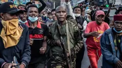 Военный с автоматом в руках идет посреди протестующих