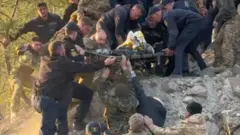 Фото в карʼєрі, багато чоловіків тримають ноші, інші знизу підтримують тих, хто зверху