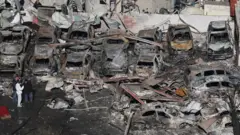 Pessoas caminham entre os destroços de carros e um prédio destruído em um ataque aéreo israelense no bairro de Corniche el-Mazraa, em Beirute.