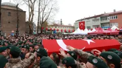Albayrak'ın Türk bayrağına sarılı tabutu özel harekat polisleri tarafından taşınıyor. Tabutun etrafında büyük bir kalabalık var. Çevredeki binalarda Türk bayrakları asılı.