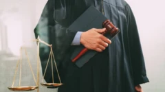 Juiz com toga preta segurando um martelo e um processo, ao lado de uma balança da justiça.