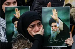 Bir başörtülü kadın elinde Hamaney'in fotoğrafını taşıyor. Tek eliyle de ağzını kapatmış ve ağlar gibi bakıyor.