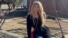 Женщина с длинными светлыми волосами сидит на детской площадке и улыбается