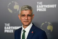 Sadid Khan posa para foto usando um terno azul e gravata verde. Atrás dele está um painel do prêmio Earthshot