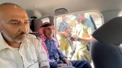 Ibrahim y Mohamed sentados dentro de un auto, junto al que están parados soldados israelíes