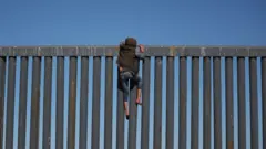 потенциальный нелегальный иммигрант пытается перелезть в США через заграждение на мексиканской границе, 2018 год
