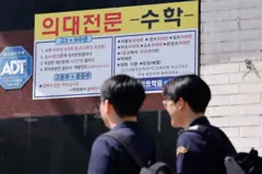 두 학생이 학원 간판이 걸린 거리를 걷고 있다