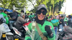 Seorang perempuan pengemudi ojol sedang membawa dua kuntum mawar.