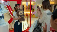 Uma jovem tira fotos com um brinquedo Labubu na loja pop-up