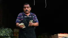 Homem segura dólares nas mãos, em um mercado de El Salvador
