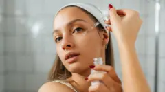 Młoda kobieta stoi w łazience i nakłada na twarz serum