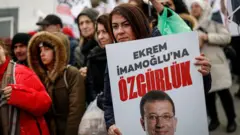 İmamoğlu'na Özgürlük posteri tutan bir kadın gerisinde bir grup insan yürüyüş yapıyor.