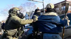 Agenta ICE - eden je nosil plinsko masko, drugi pa masko za obraz - sta aretirala osebo, za katero se je zdelo, da drži nekakšno palico ali orožje.