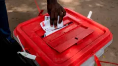 Hand of man wey wan drop vote inside ballot box