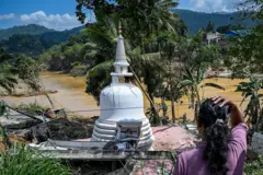 TOPSHOT - A woman looks at a stupa lying in a damaged state following the landslides in the aftermath of Cyclone Ditwah in Gampola town, in Kandy district on December 4, 2025. Tropical storms and monsoon rains have pummelled Southeast and South Asia this month, triggering landslides and flash floods from the rainforests of Indonesia's western Sumatra island to highland plantations in Sri Lanka. (Photo by Ishara S. KODIKARA / AFP via Getty Images)