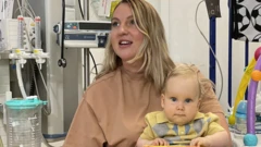 Megan sostiene a Edward en su regazo, en un cuarto de hospital