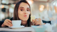 Mujer con una taza de café en una mano y una reproducción de un diente en otra.