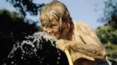 Un niño toma agua de una manguera