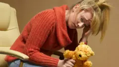 mujer con cara de angusta con un oso de peluche en su mano