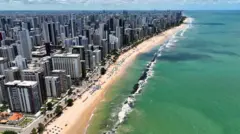 Foto aérea mostra prédios e praiawww arenaesportiva betRecife