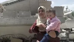 Раҳима Набҳан вайрон бўлган уйи олдида очиқ ҳавода ухлаётганларини айтади