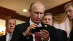 Vladimir Putin examines an iPhone in the company of spokesman Dmitri Peskov (right) and Foreign Minister Sergei Lavrov (left)