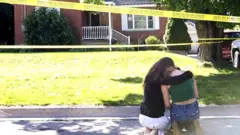 Two women console each other outside the house where the shooting took place