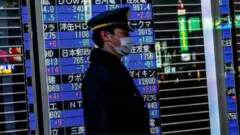 A passerby with a face mask walks past a stock board in Tokyo's Nihonbashi district showing the Nikkei average index falling on the Tokyo Stock Exchange.