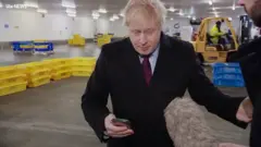 Boris Johnson olha finalmente a imagem no celular do repórter Joe Pike