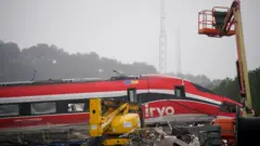 Una grúa amarilla intenta levantar uno de los vagones rojos del tren Iryo.