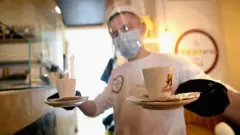 Официант в медицинской маске и с двумя чашками кофе