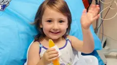 Cleo Smith waves from a hospital bed after her rescue