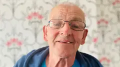 Um homem de cabelos grisalhos e usando óculos sorri para a câmera