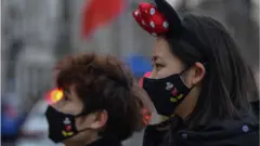 Deux clients portant des masques Mickey Mouse dans un parc Disney