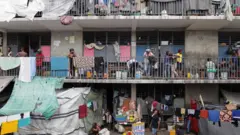Una escuela que se utiliza como refugio, con gente parada en balcones, ropa tendida y refugios improvisados hechos con lonas, en Puerto Príncipe, octubre de 2025.