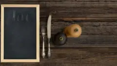 Sobre la mesa, sal, pimienta, cubiertos y un menú.