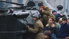 Romanian soldiers and civilians take cover behind a tank in Bucharest's Palace Square in December 1989