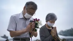 An elderly couple prays for victims in front of a cenotaph at Peace Memorial Park in Hiroshima