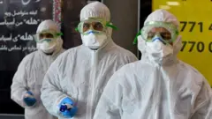 A medical team wearing protective outfit awaits to check Iraqi passengers returning from Iran