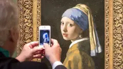 Un hombre toma una foto del cuadro La joven de la perla de Johannes Vermeer