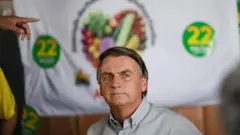 Bolsonaro olhando para o lado, em frente a pano com adesivos e seu número de campanha
