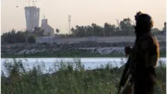 (أرشيف) أحد أفراد الأمن العراقي وفي الخلفية المنطقة الخضراء التي توجد بها السفارة الأمريكية