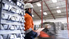 Trabalhador ao lado de barras de alumínio