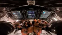 En el interior de la cápsula Orion, los astronautas Reid Wiseman (izq.), comandante, y Victor Glover (der.), piloto, preparan la nave espacial Orion para el reingreso a la Tierra.