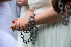 Menor de idade vestida de noiva com as mãos acorrentadas