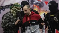 Combatentes do Hamas escoltam o refém israelense Tal Shoham antes de entregá-lo à Cruz Vermelha em Rafah